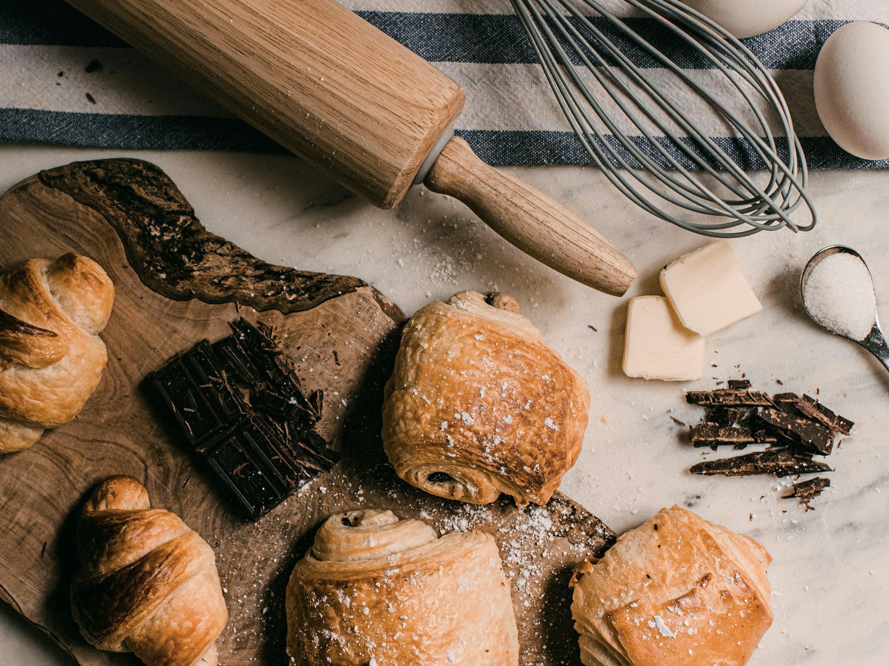 Home Freshly baked croissants and chocolate pastries on a wooden board with baking tools